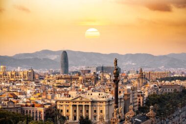 Sunset over Barcelona skyline featuring the Columbus Monument, Torre Glòries, and historic city architecture.