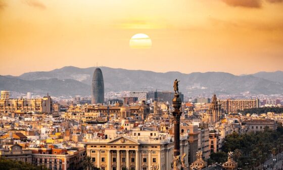 Sunset over Barcelona skyline featuring the Columbus Monument, Torre Glòries, and historic city architecture.